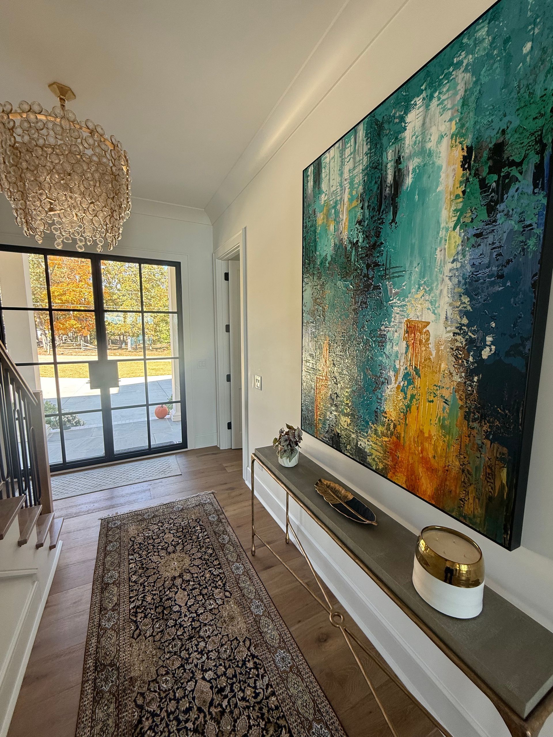 Hallway with large abstract painting, chandelier, window, long rug, and console table.