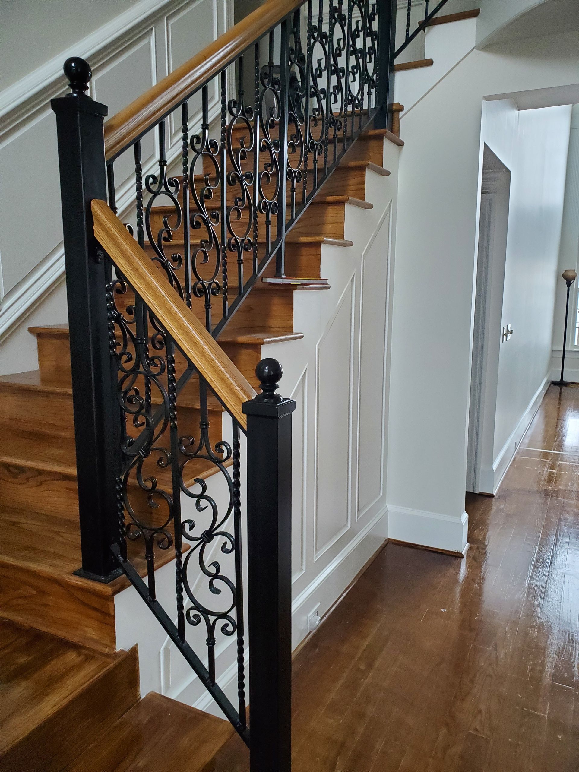 Wooden staircase with ornate black iron railing.