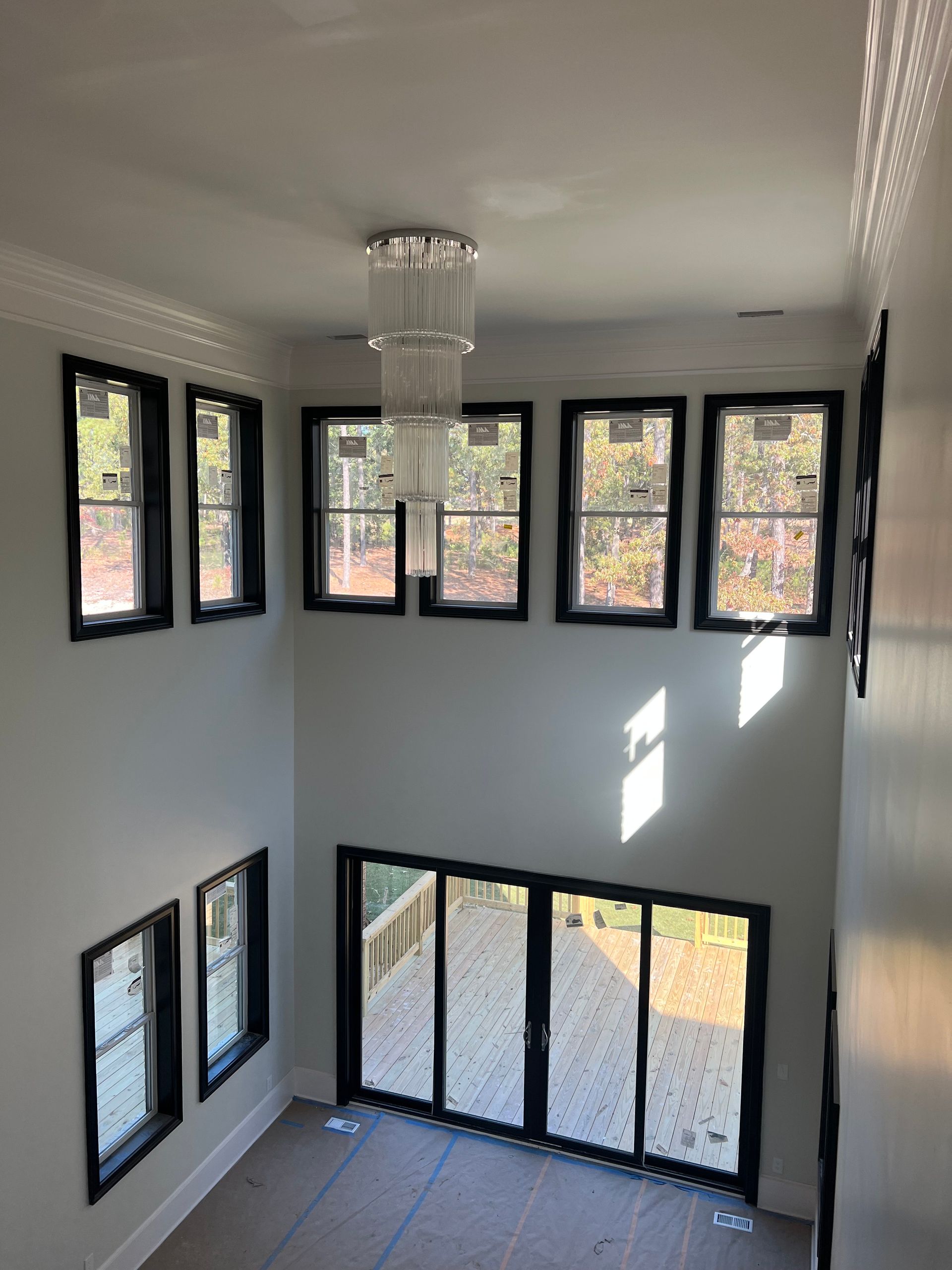 Interior view of a two-story space with black-framed windows, a chandelier, and glass doors to a backyard.