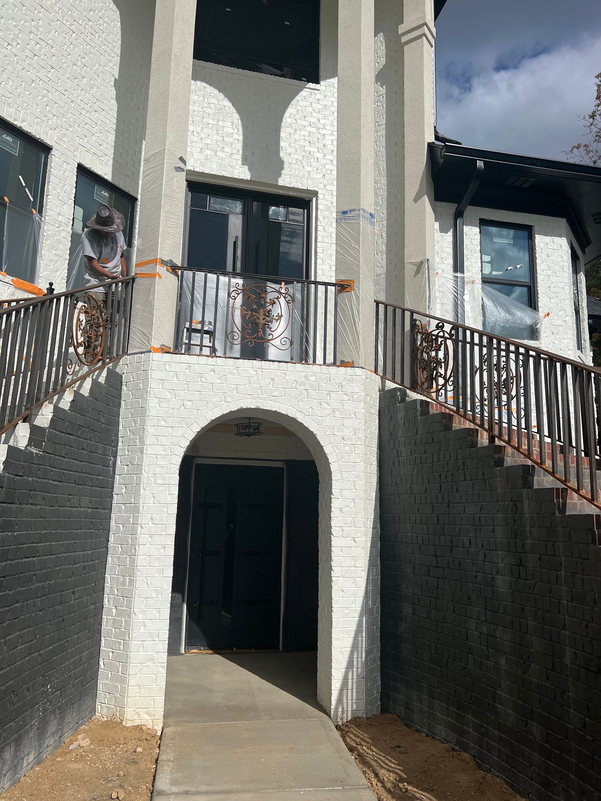 White brick building with arched doorway and black trim, wrought iron railings and stairs.