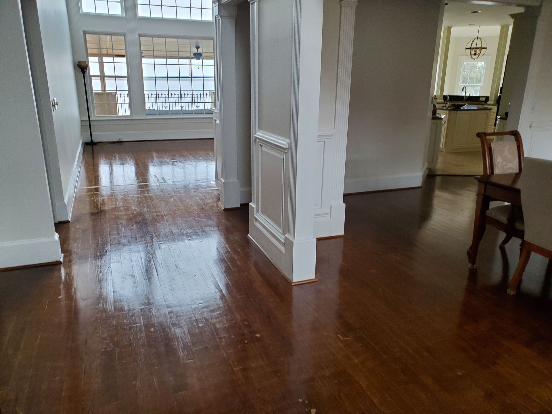 Hardwood floors in a home, reflecting light. White columns and kitchen in the background.