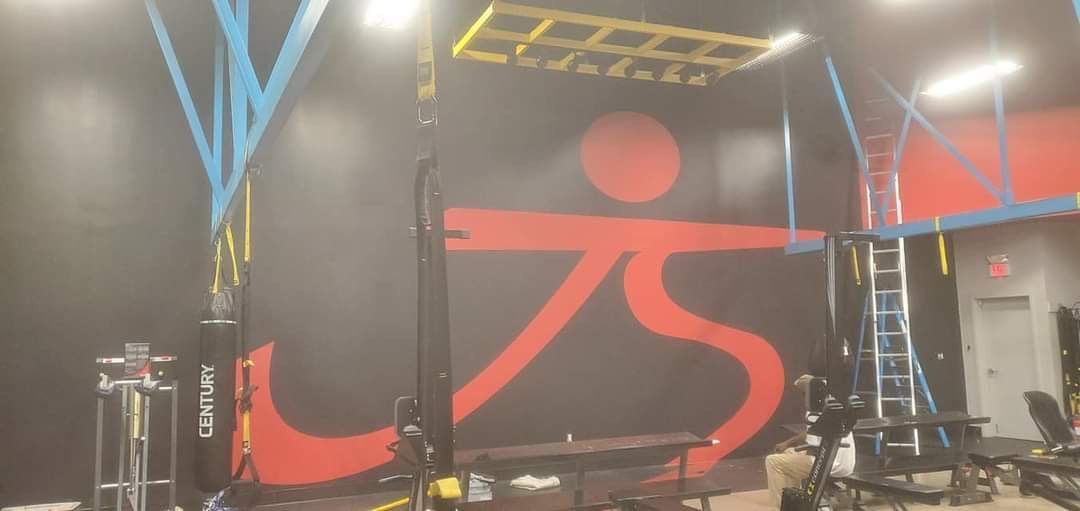 Gym interior with a red and black logo on the wall and various workout equipment.