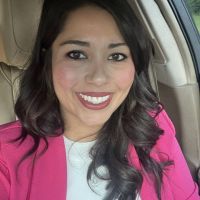 A woman in a pink jacket is smiling while sitting in a car.