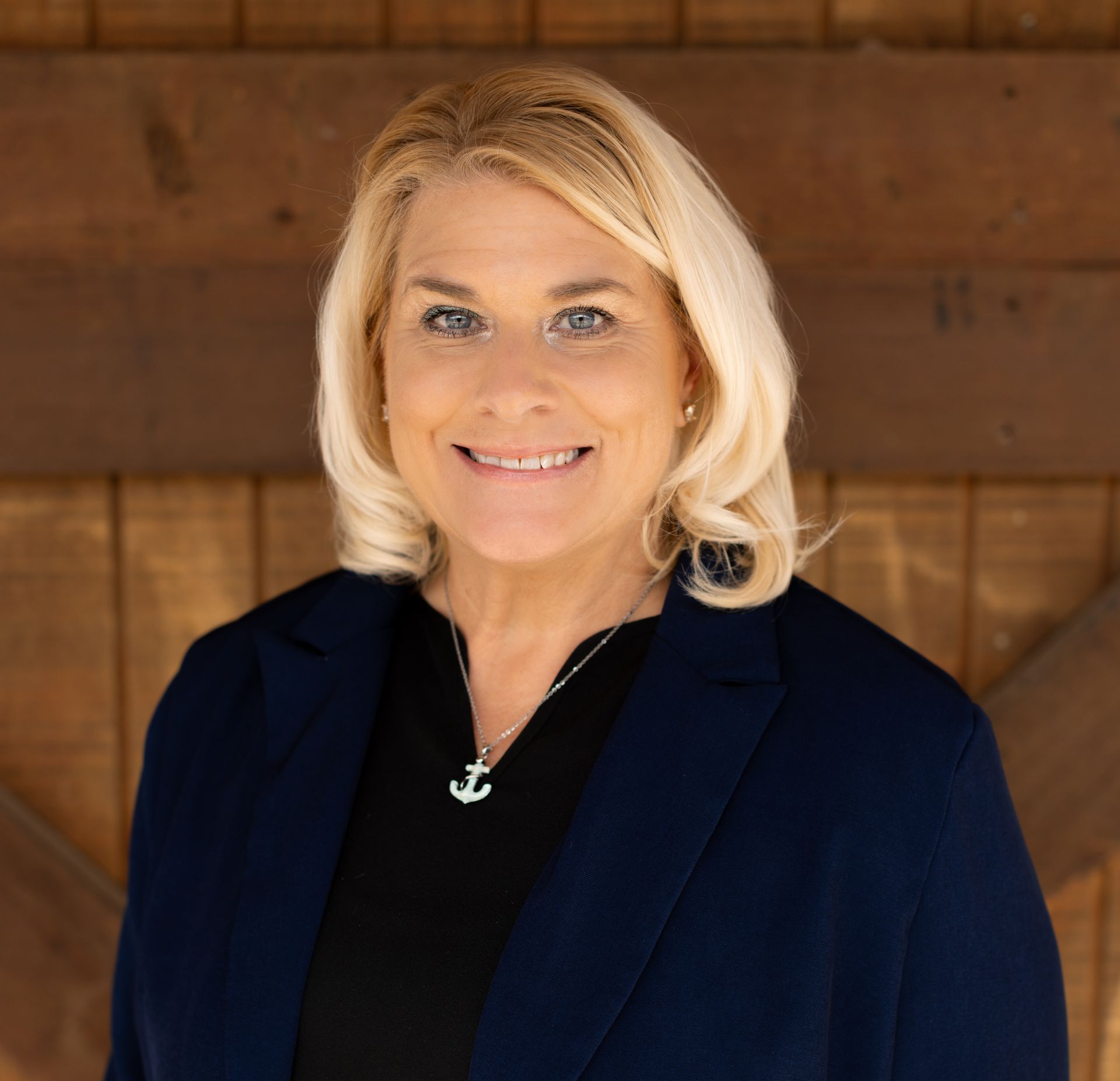 A woman in a blue shirt and necklace is smiling for the camera.