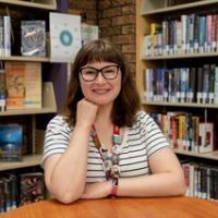 A woman wearing glasses is sitting at a table in a library.