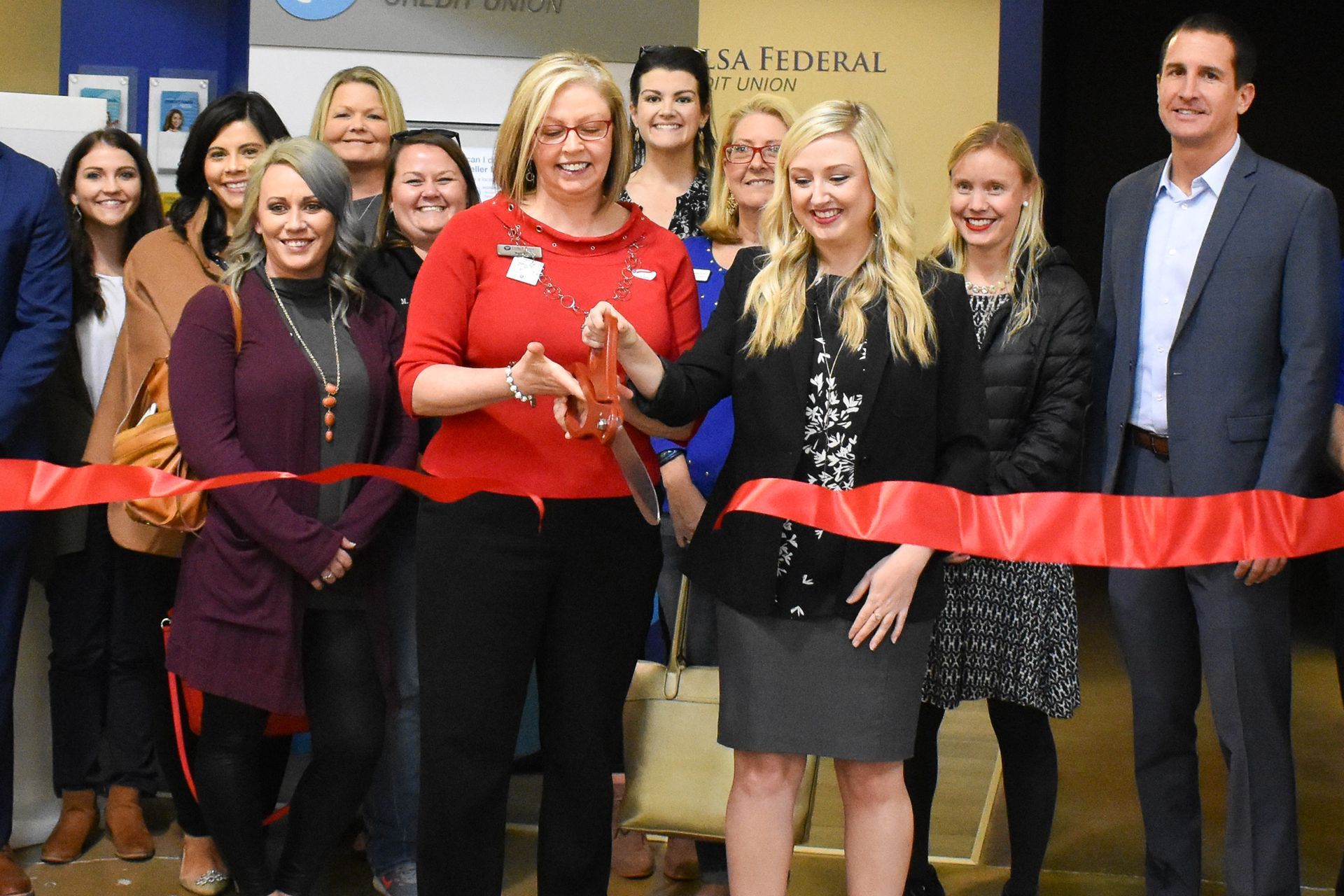 A group of people are standing around a woman cutting a red ribbon.