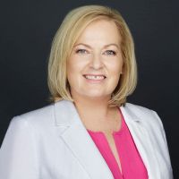 A woman in a white jacket and pink shirt is smiling for the camera.