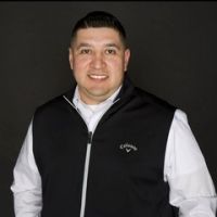 A man wearing a black vest and a white shirt is standing in front of a black background.