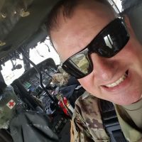 A man in a military uniform and sunglasses is taking a selfie in the cockpit of a helicopter.