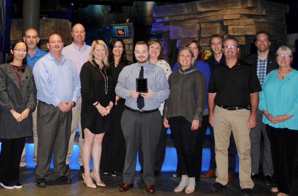 A group of people are posing for a picture with a man holding an award.