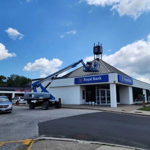 A construction lift reaches toward the roof of a Royal Bank building under a blue sky with white clouds.