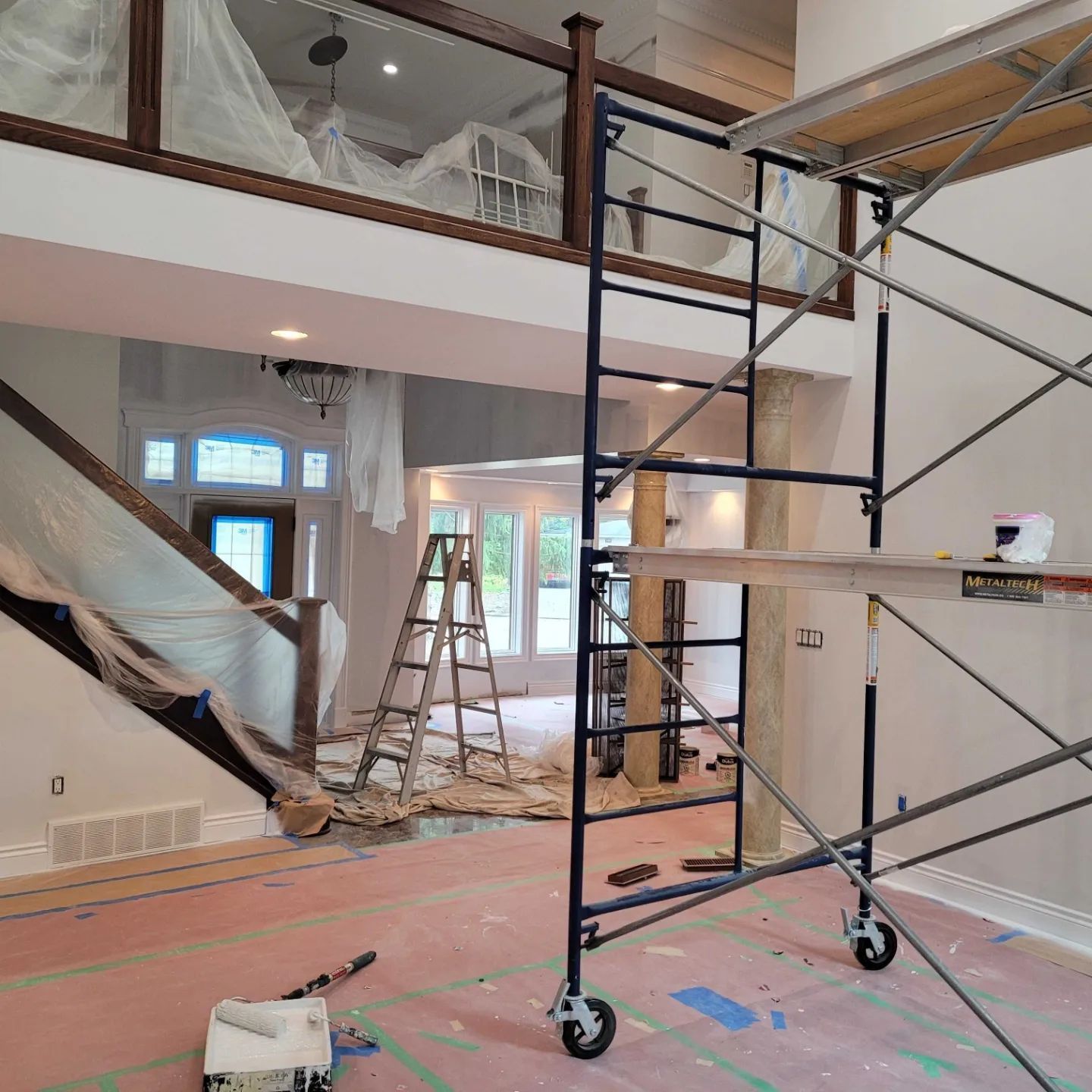 Interior of a large home under renovation, featuring a tall metal scaffold, a wooden stepladder, and plastic-covered walls.