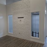 A white-painted brick wall featuring a centered cutout niche, flanked by two narrow windows in a room with wood flooring.