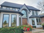 A large, two-story white house with dark window frames, a prominent arched entryway, and a sprawling front garden.