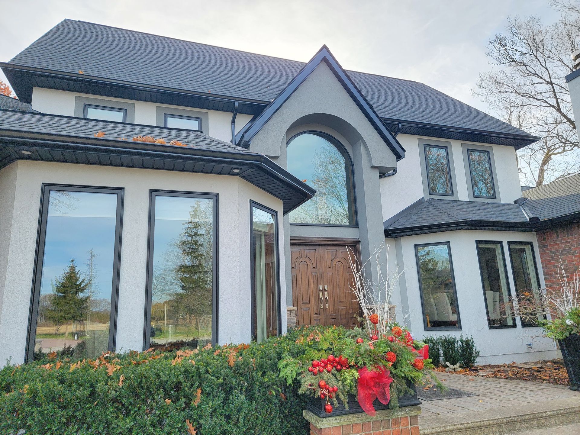 A large, two-story white house with dark window frames, a prominent arched entryway, and a sprawling front garden.