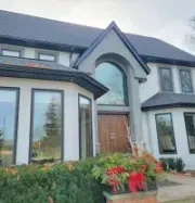 A large, two-story white house with dark window frames, a prominent arched entryway, and a sprawling front garden.