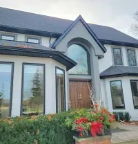 A large, two-story white house with dark window frames, a prominent arched entryway, and a sprawling front garden.