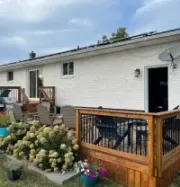 A white brick house with a large wooden deck, patio furniture, and white hydrangea bushes in the backyard.