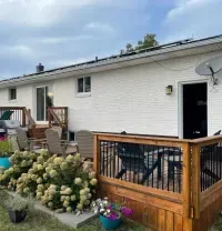 A white brick house with a large wooden deck, patio furniture, and white hydrangea bushes in the backyard.