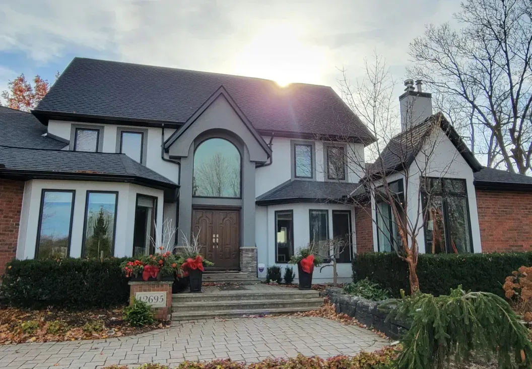 A two-story house with a white stucco and red brick exterior, dark grey roof, arched entryway, and landscaped front yard.