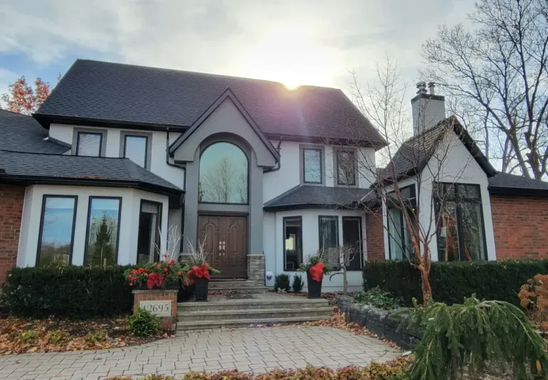 A two-story house with a white stucco and red brick exterior, dark grey roof, arched entryway, and landscaped front yard.