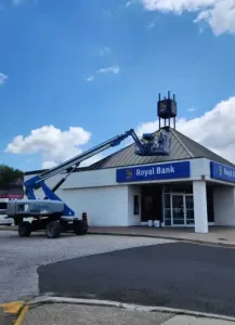 A construction lift reaches toward the roof of a Royal Bank building under a blue sky with white clouds.