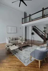 Modern, high-ceiling living room with wood floors, a neutral sofa, patterned rug, armchairs, and a wooden staircase.