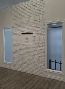 A white-painted brick wall featuring a centered cutout niche, flanked by two narrow windows in a room with wood flooring.