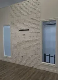 A white-painted brick wall featuring a centered cutout niche, flanked by two narrow windows in a room with wood flooring.