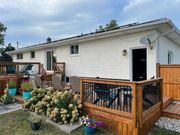 A white brick house with a large wooden deck, patio furniture, and white hydrangea bushes in the backyard.