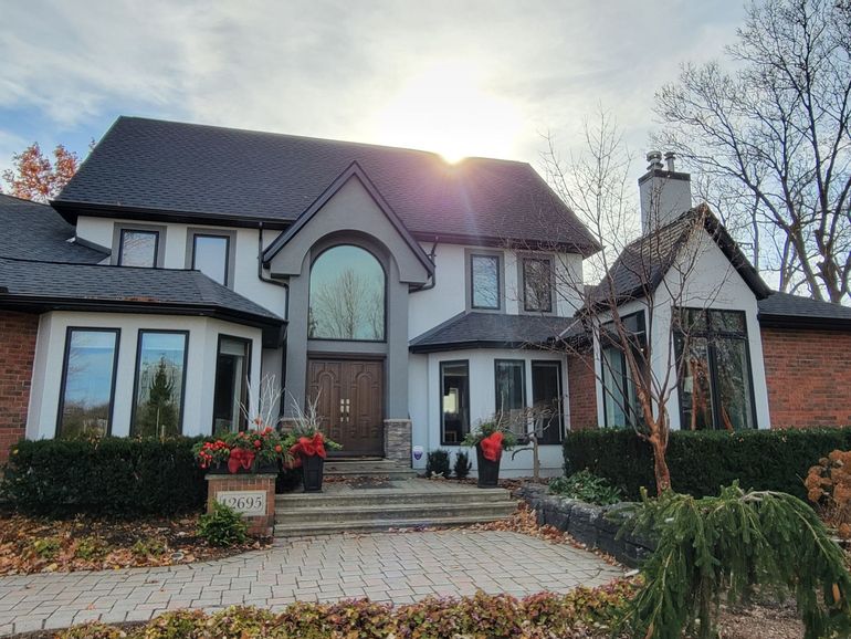 A two-story house with a white stucco and red brick exterior, dark grey roof, arched entryway, and landscaped front yard.