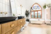 A luxury bathroom with a fluted wooden vanity, black sinks, a freestanding clawfoot tub, and an arched stained-glass window.