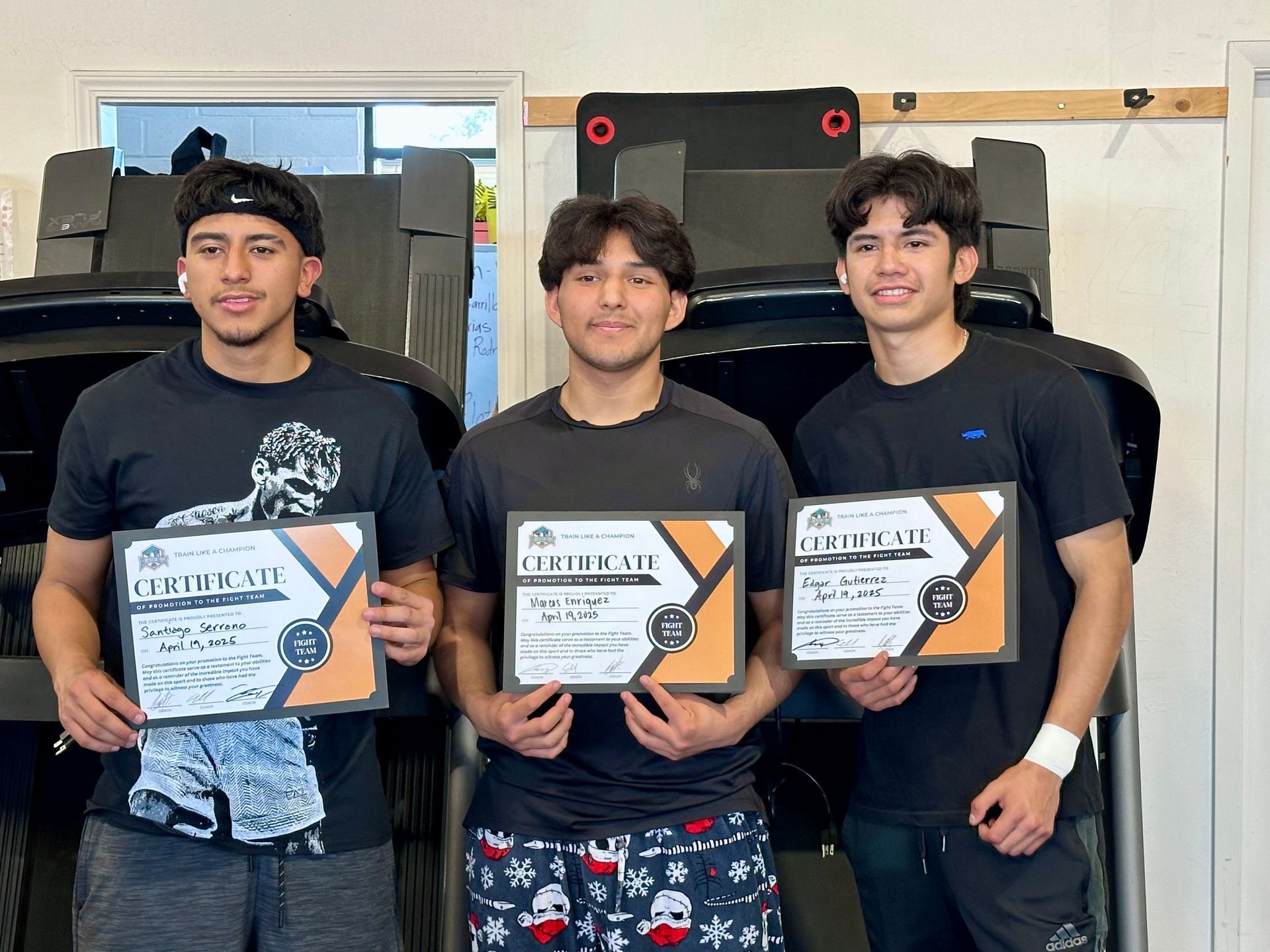 Three young men holding certificates in a gym.