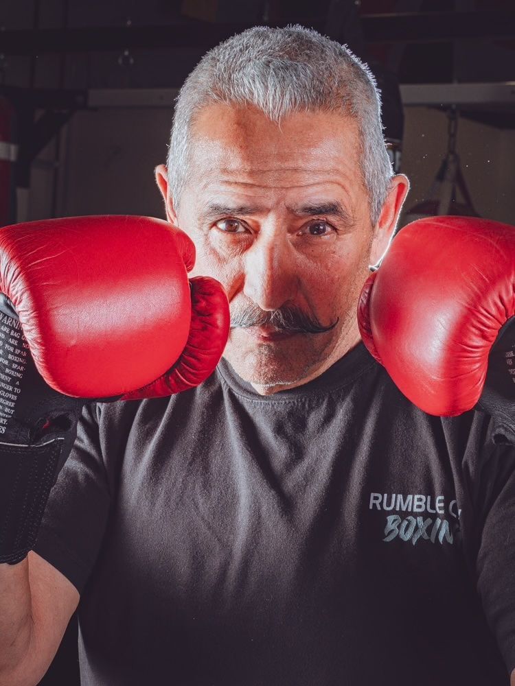 Three men in a boxing ring. One in blue, one in a jacket, and the other in black, all posed with fists up.