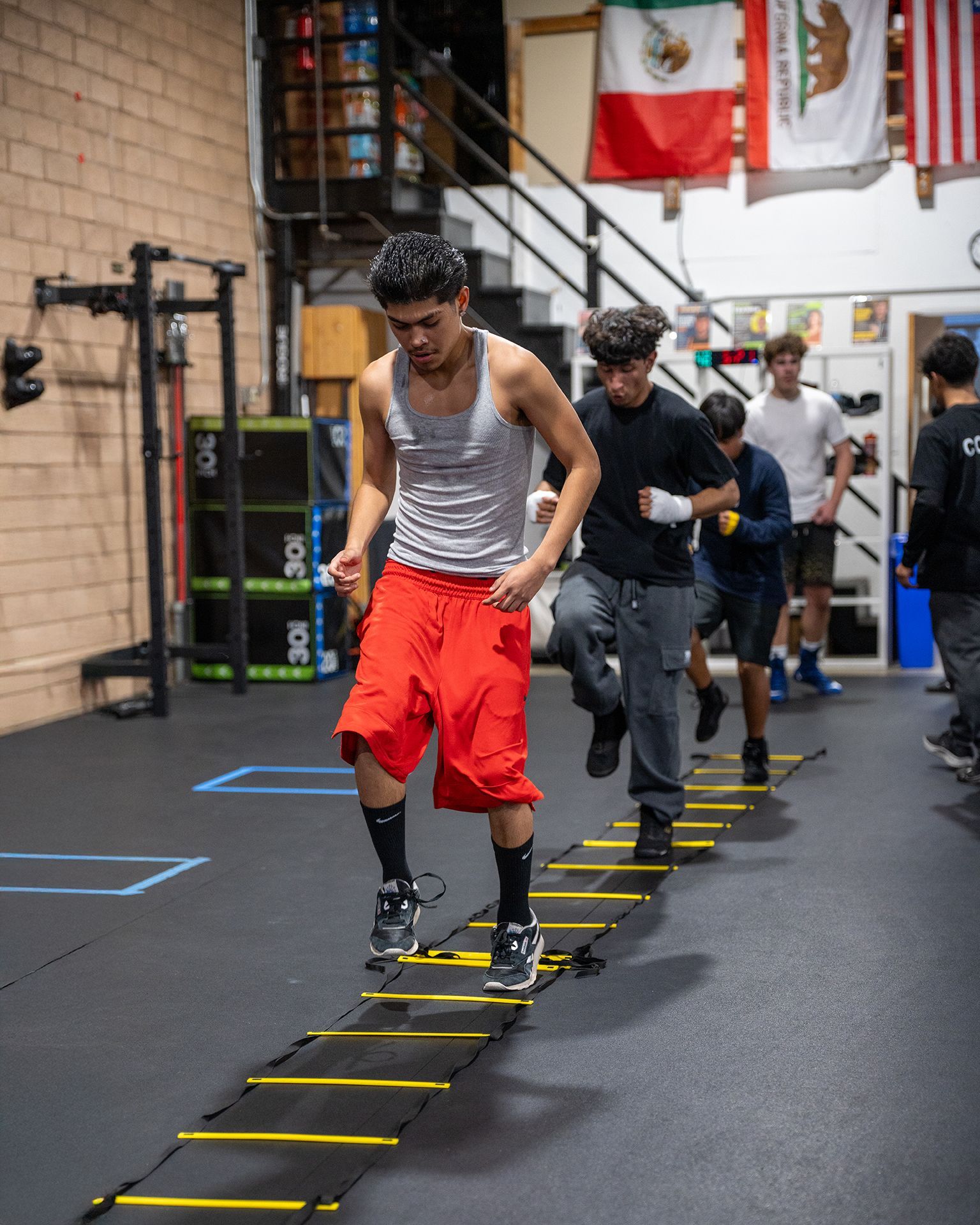 People doing agility ladder drills in a gym. Flags hang on the wall.