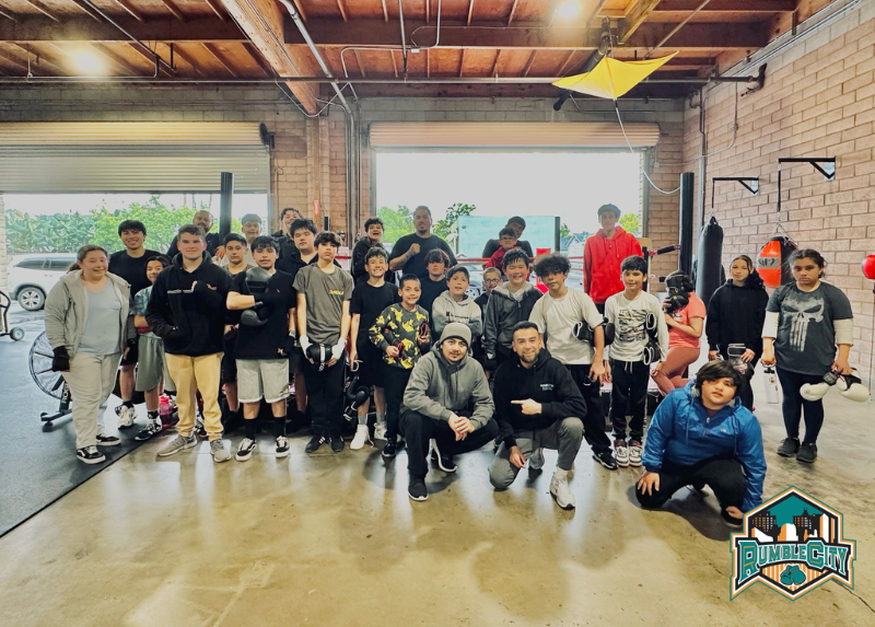Group of teens and adults pose inside a gym. Some are smiling, others are squatting. Garage door visible.