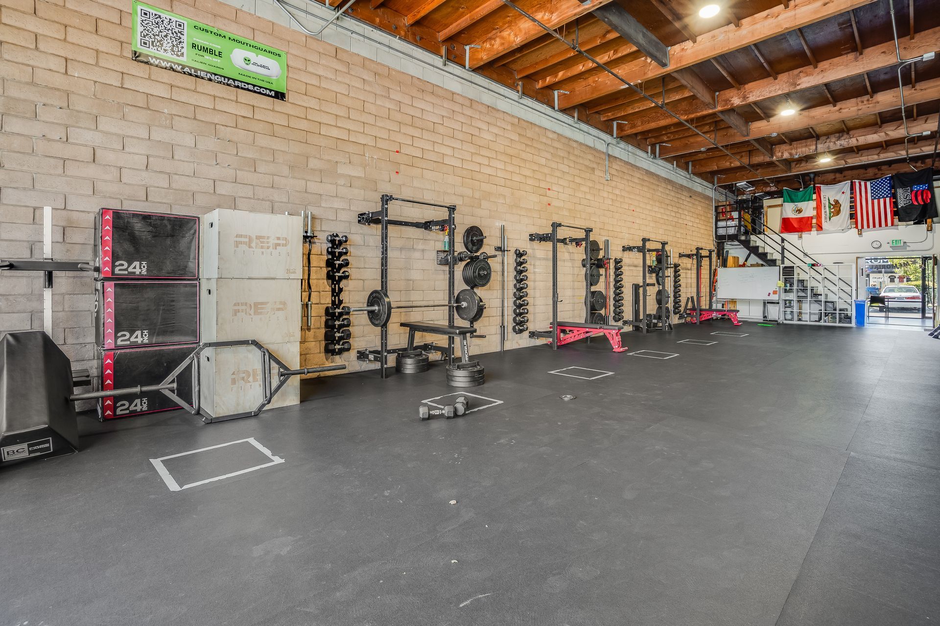 Weightlifting gym with various equipment, brick walls, and a wooden ceiling.