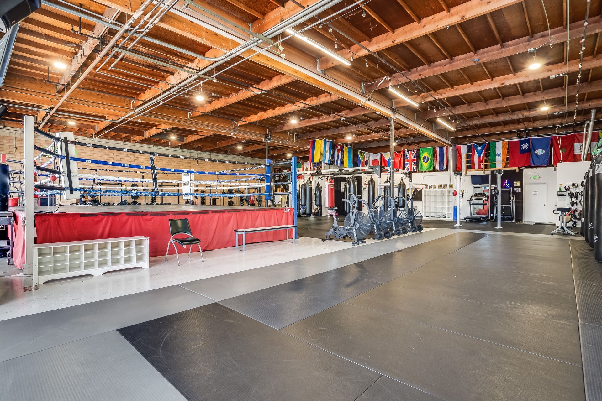 Boxing gym with a red ring, punching bags, and flags.