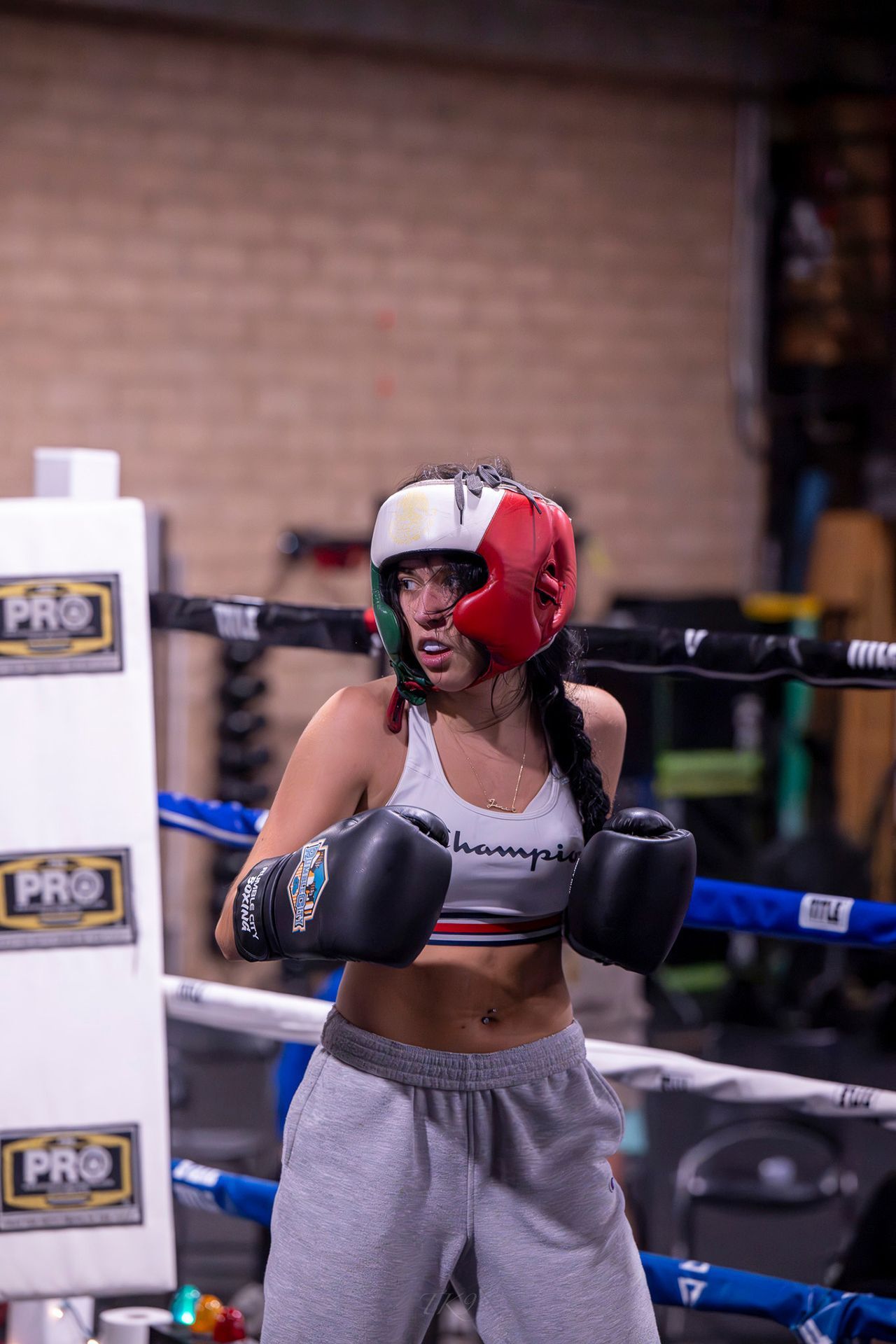 Woman in boxing ring wearing headgear, gloves, and activewear, ready to fight.