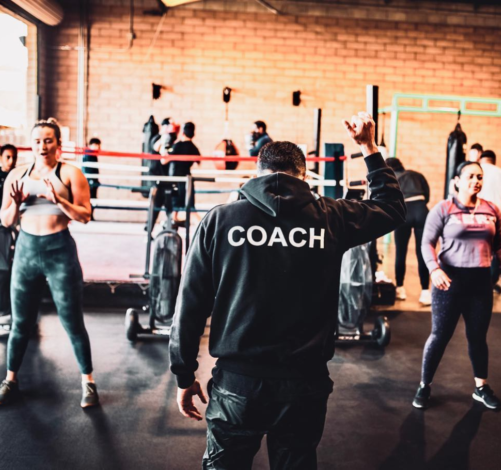 Coach leading boxing class, people exercising in gym.