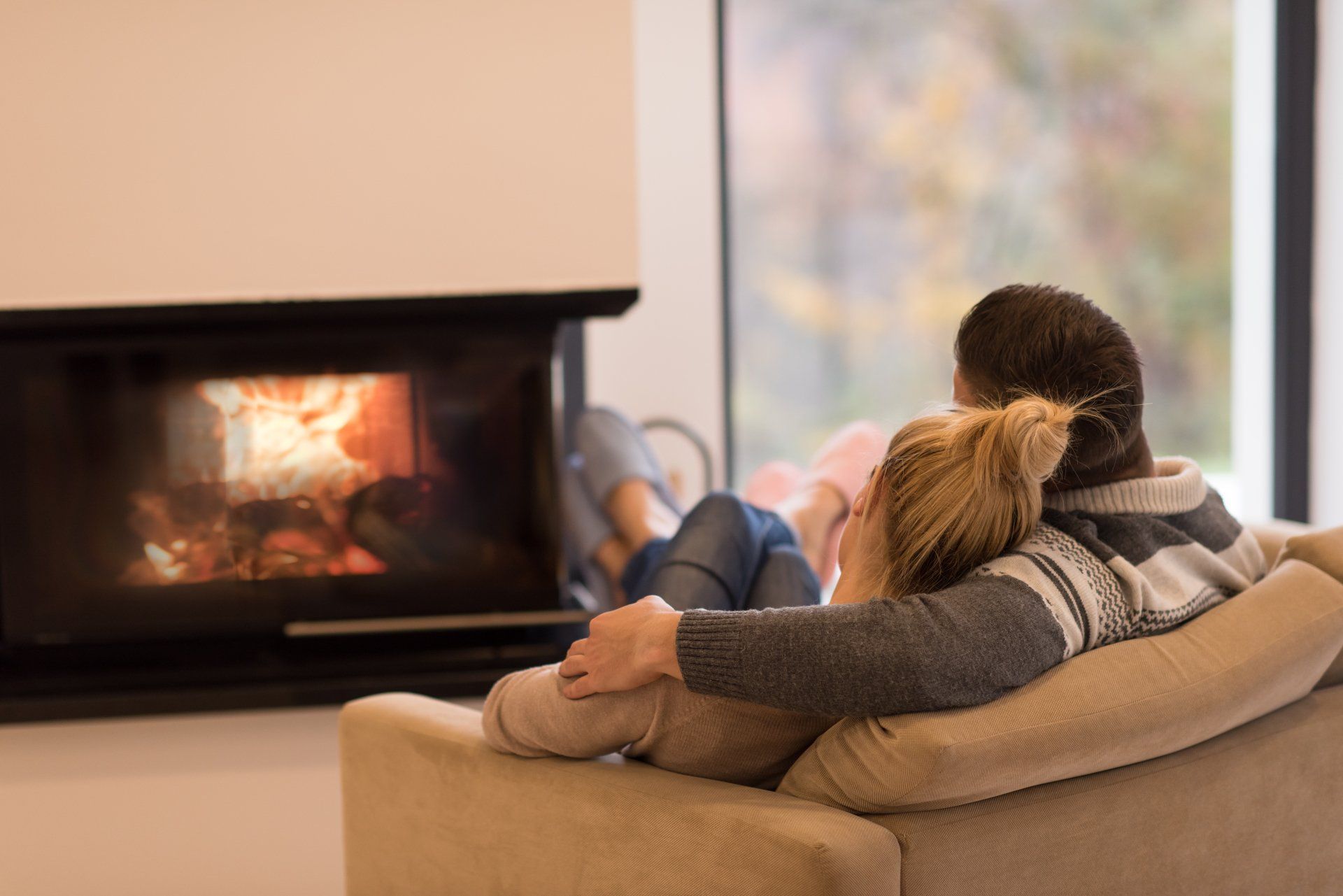 A man and a woman are sitting on a couch in front of a fireplace.