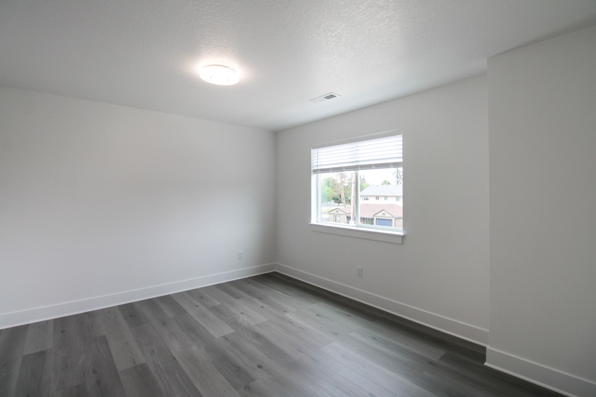 An empty bedroom with hardwood floors and a window.