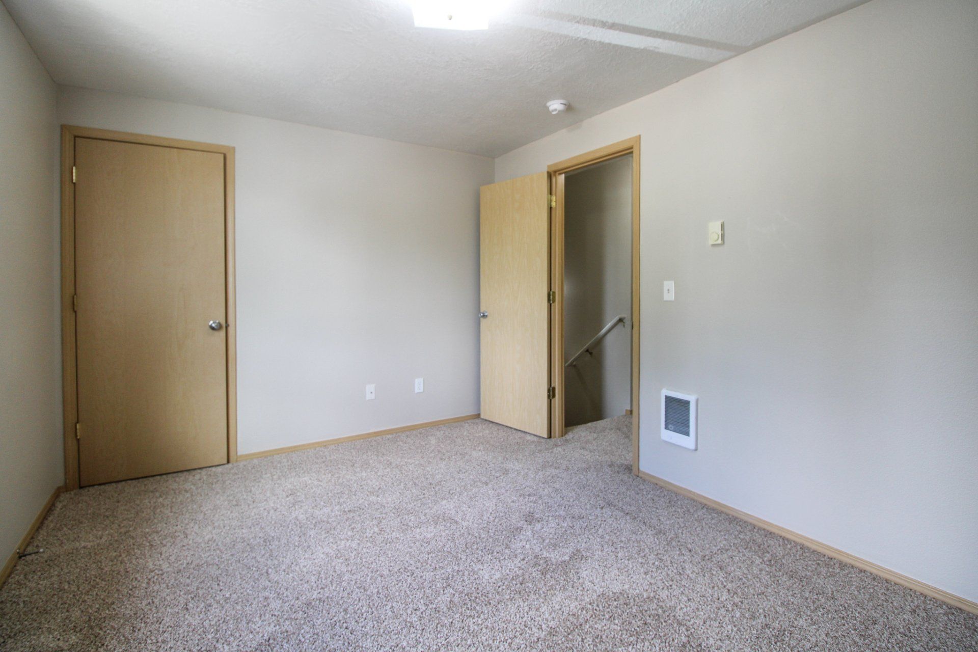 An empty room with a carpeted floor , a door , and a staircase.