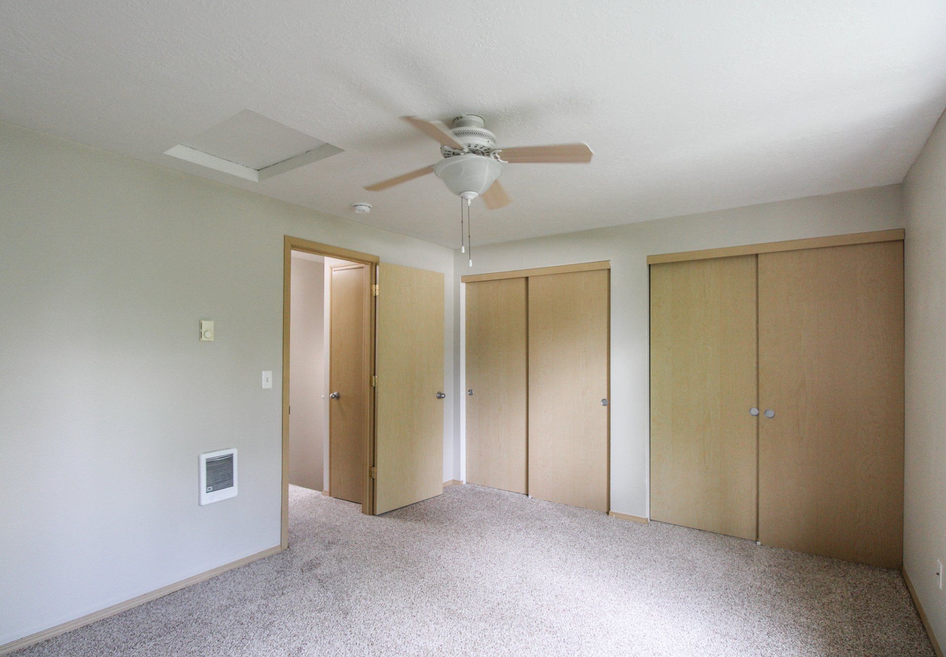 An empty bedroom with a ceiling fan and closets