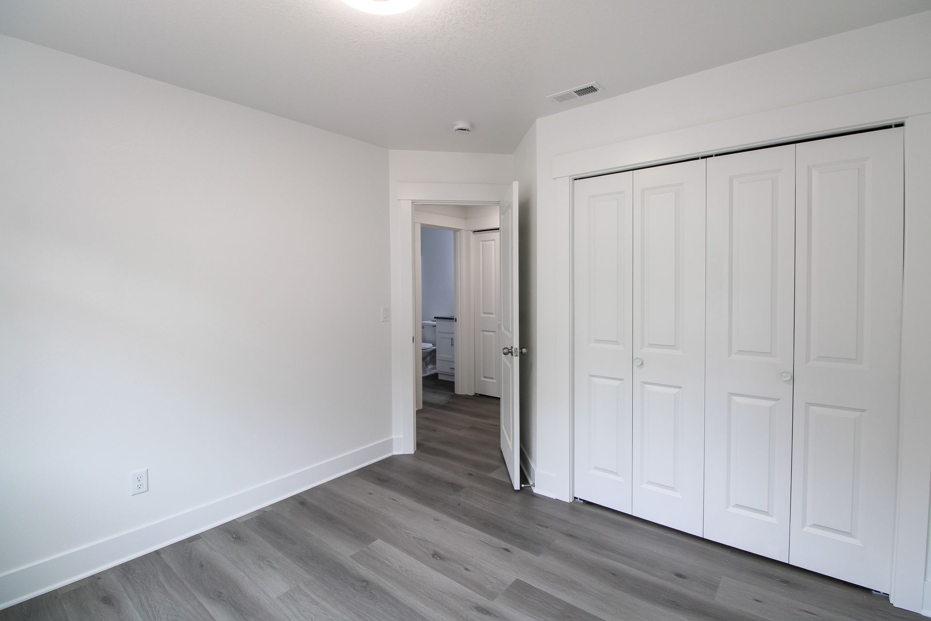 An empty bedroom with hardwood floors and white walls.