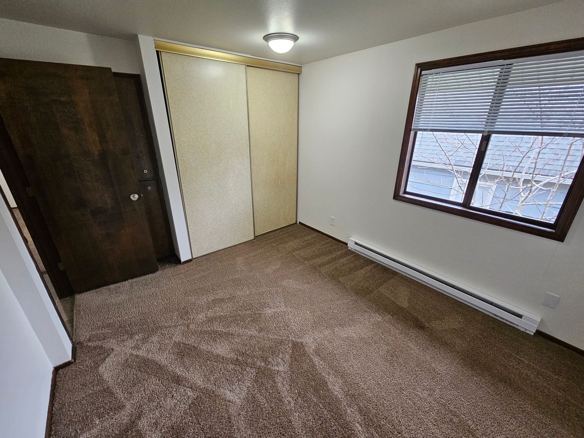 An empty bedroom with a window and a closet.