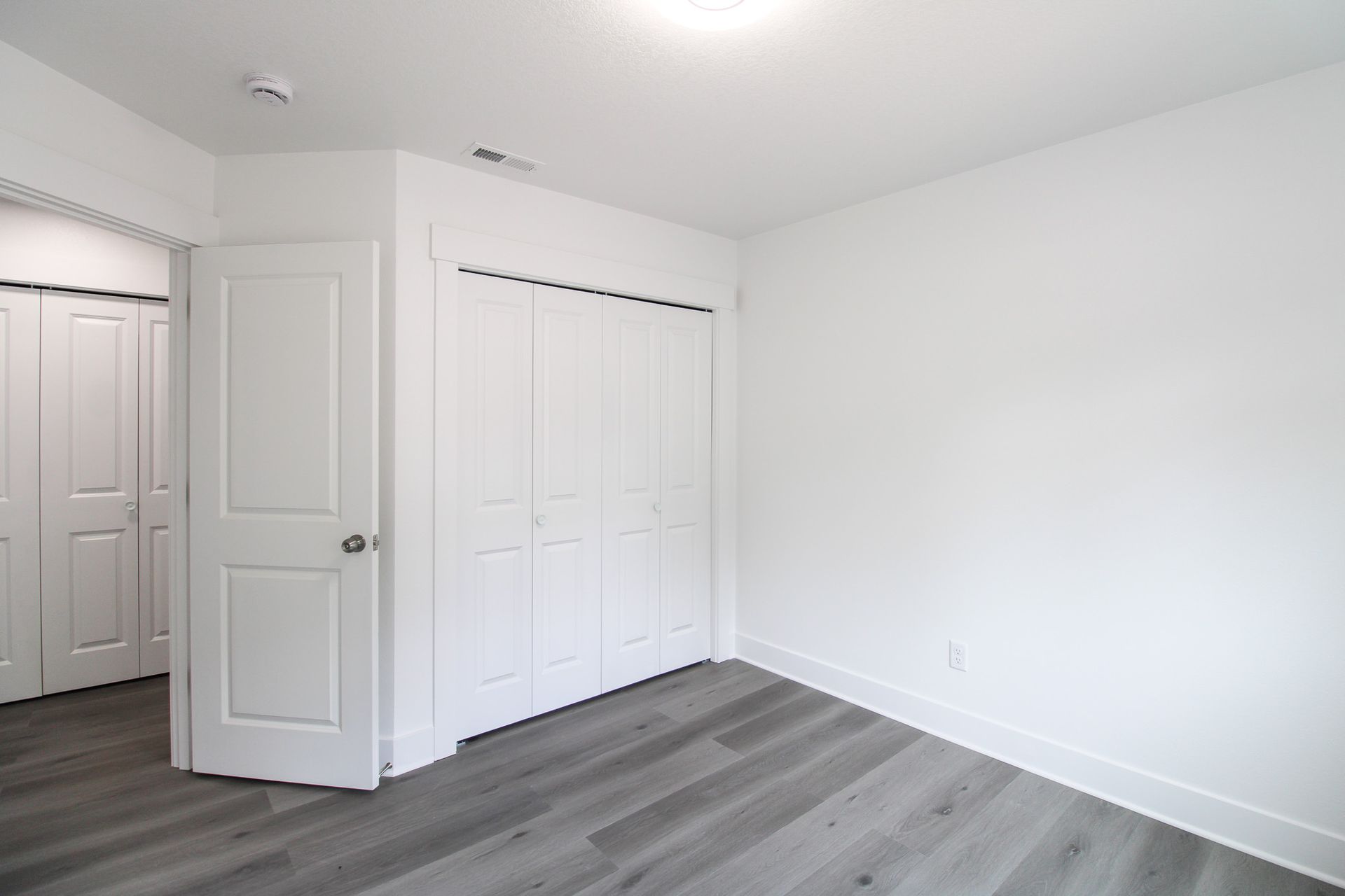 An empty bedroom with white walls and gray hardwood floors.