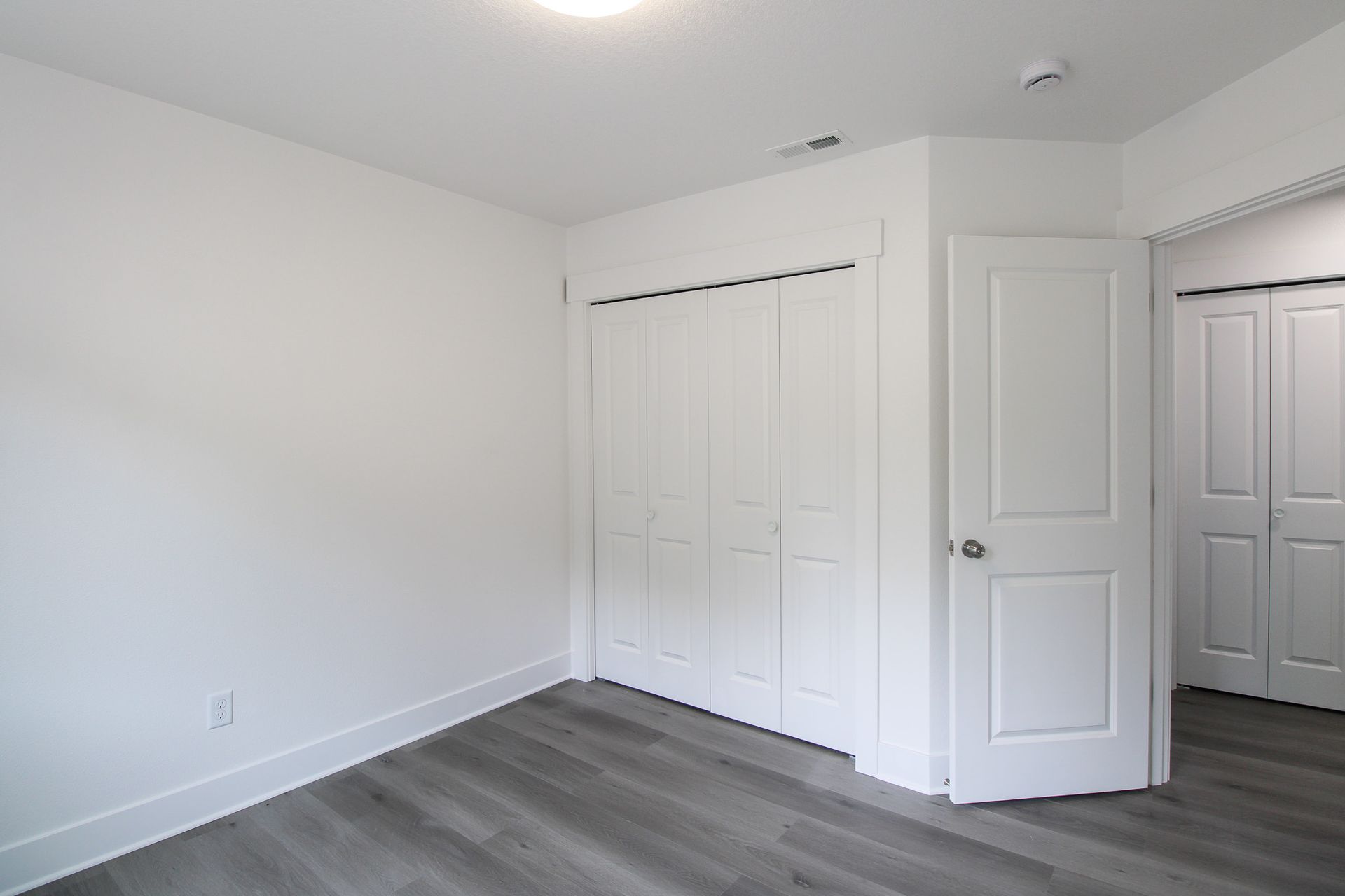 An empty bedroom with hardwood floors and white walls.