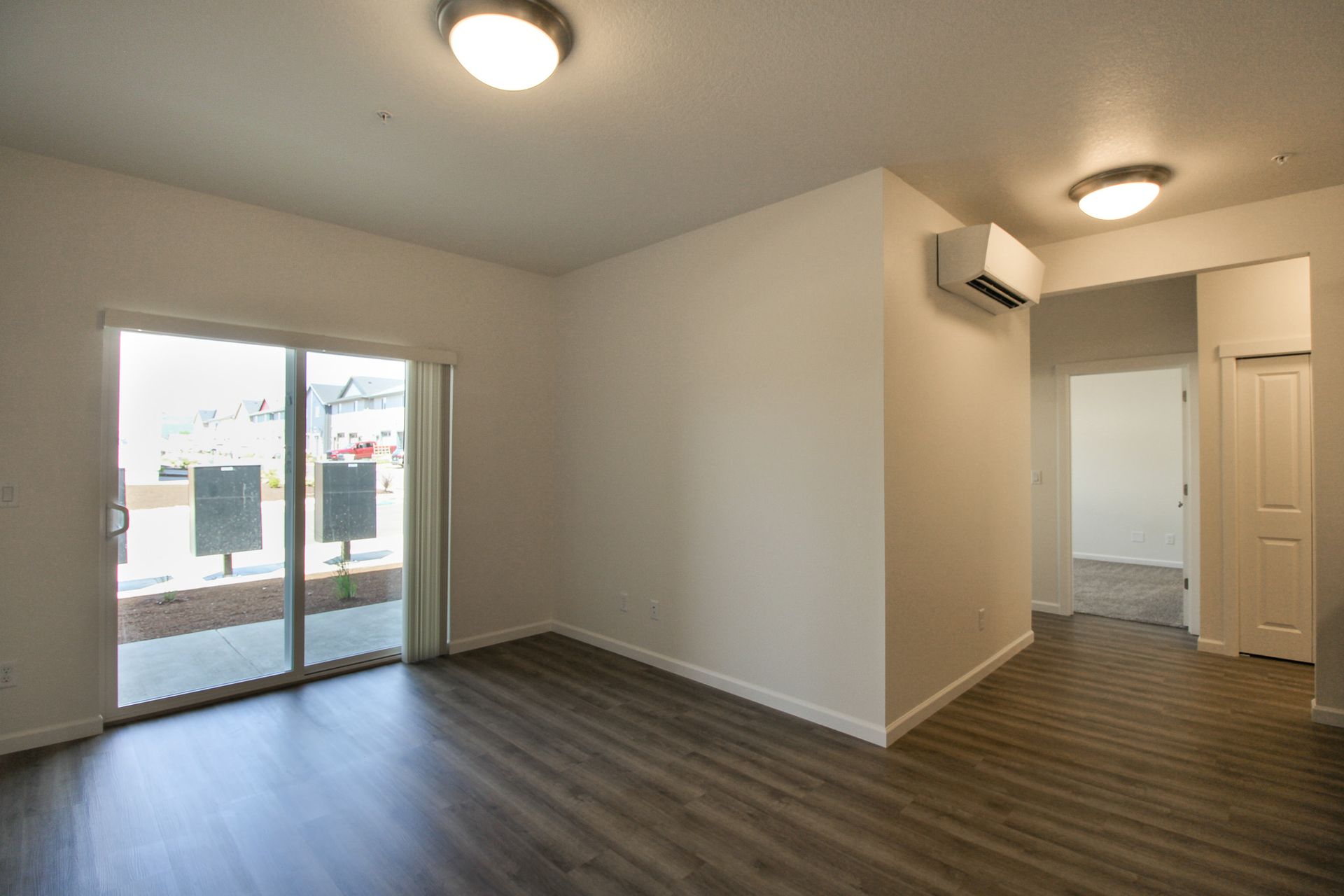 An empty living room with a sliding glass door and hardwood floors.