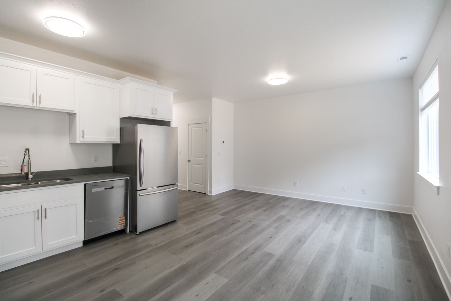 An empty living room with a kitchen and a refrigerator.
